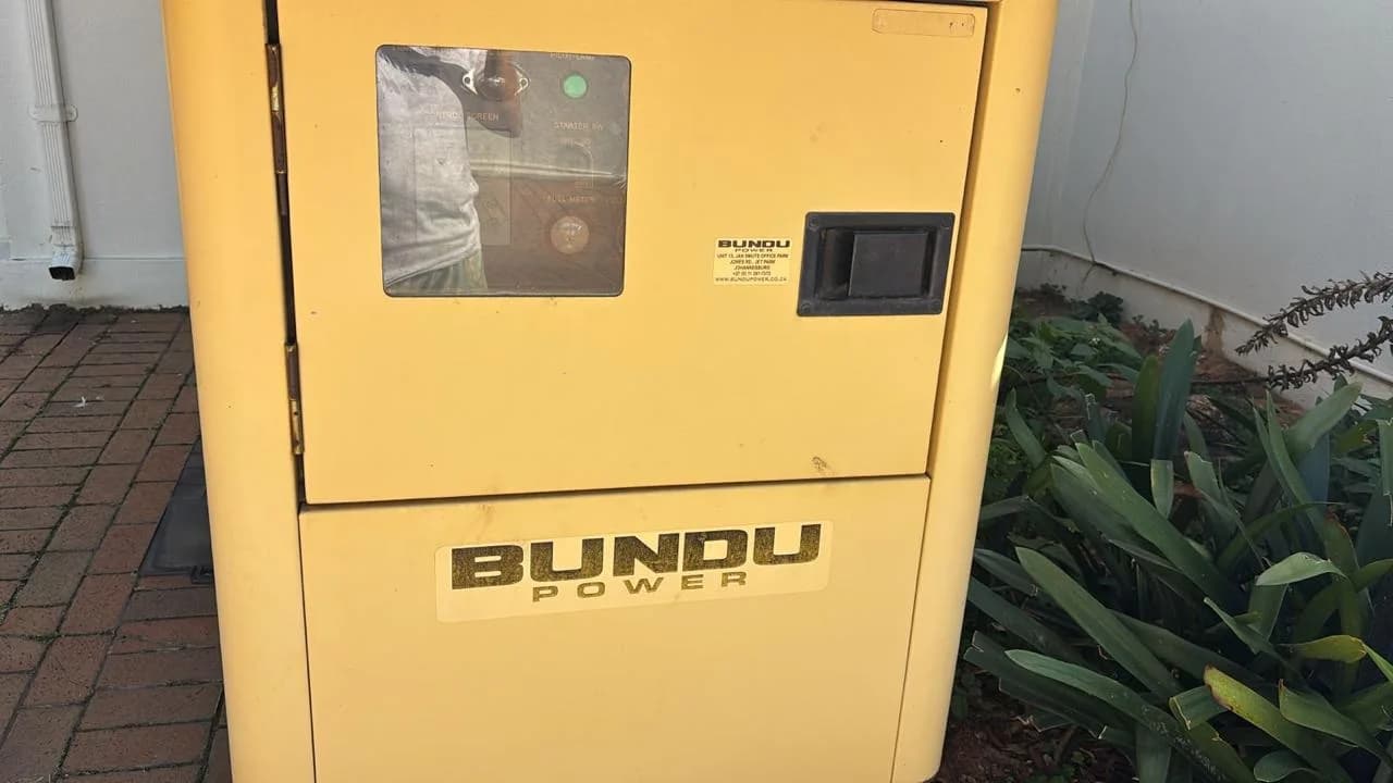 Two technicians inspecting a standby generator battery and controller during maintenance
