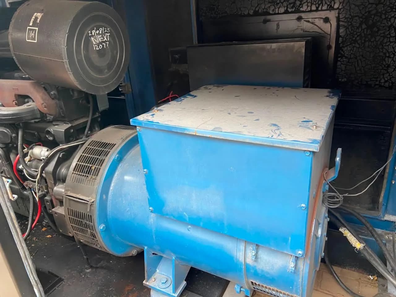 Blue alternator and engine air filter inside a soot-marked canopy, the filter marked with service date and next hours