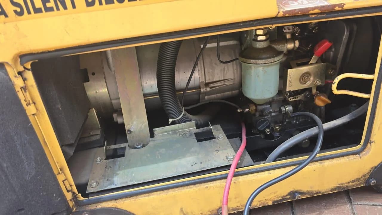 Side panel off a yellow silent diesel generator showing the fuel water separator, fuel lines and alternator