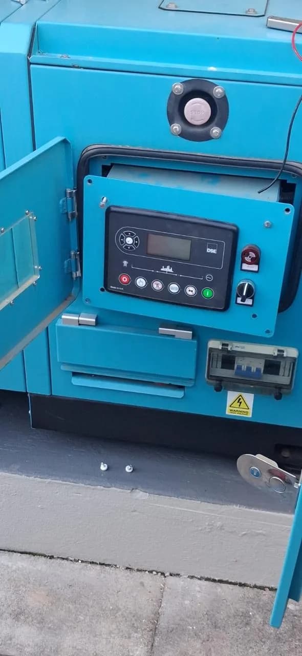 Teal canopied generator with its control door open on a DSE controller, emergency stop and output breaker