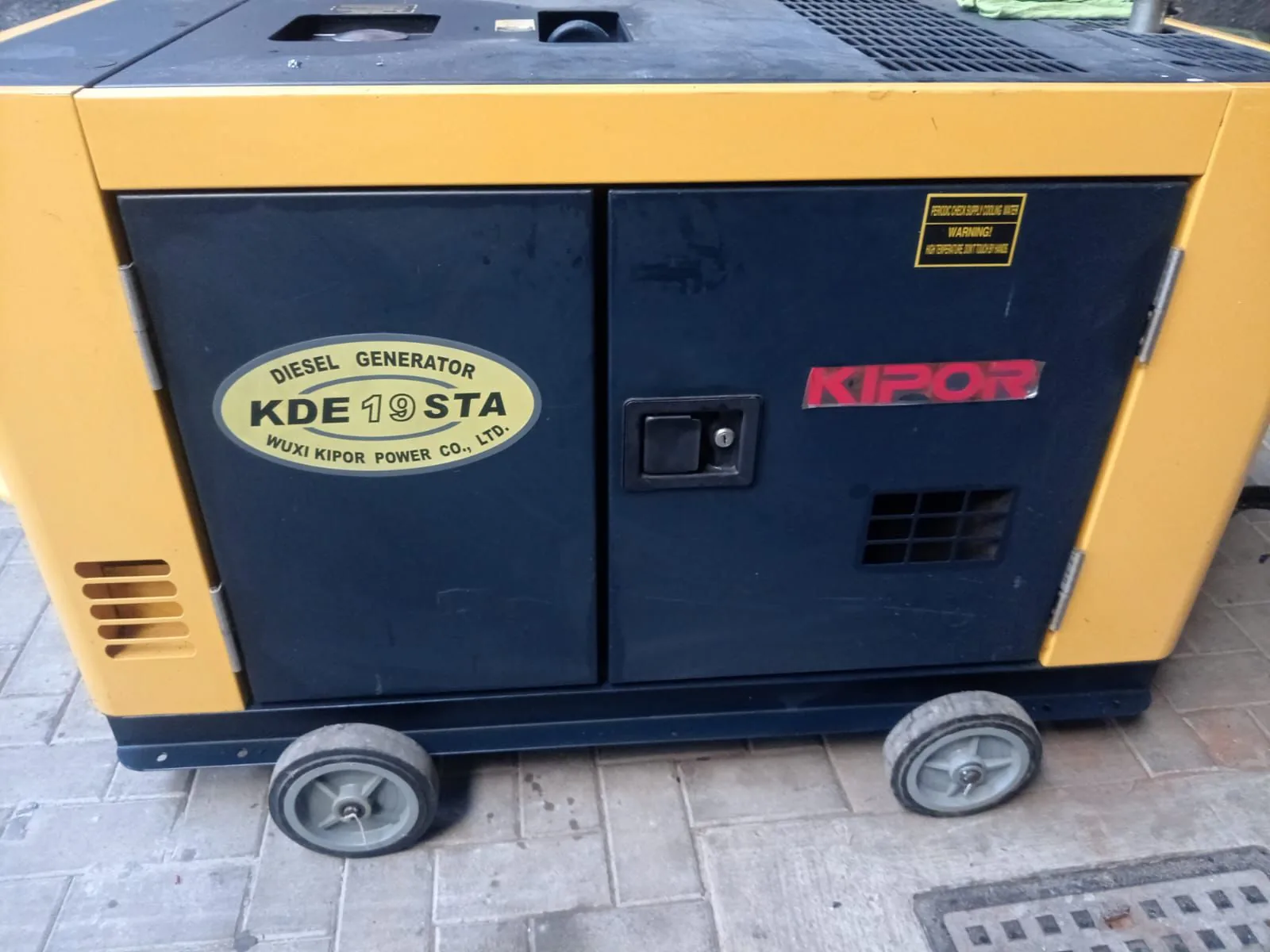 Yellow and navy Kipor KDE19STA silent diesel generator on wheels standing on paving