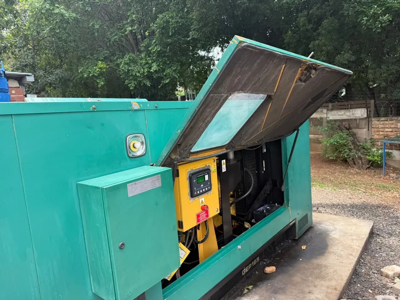 Teal canopied standby generator marked GEP165, its top hatch raised over a yellow control panel and the engine bay
