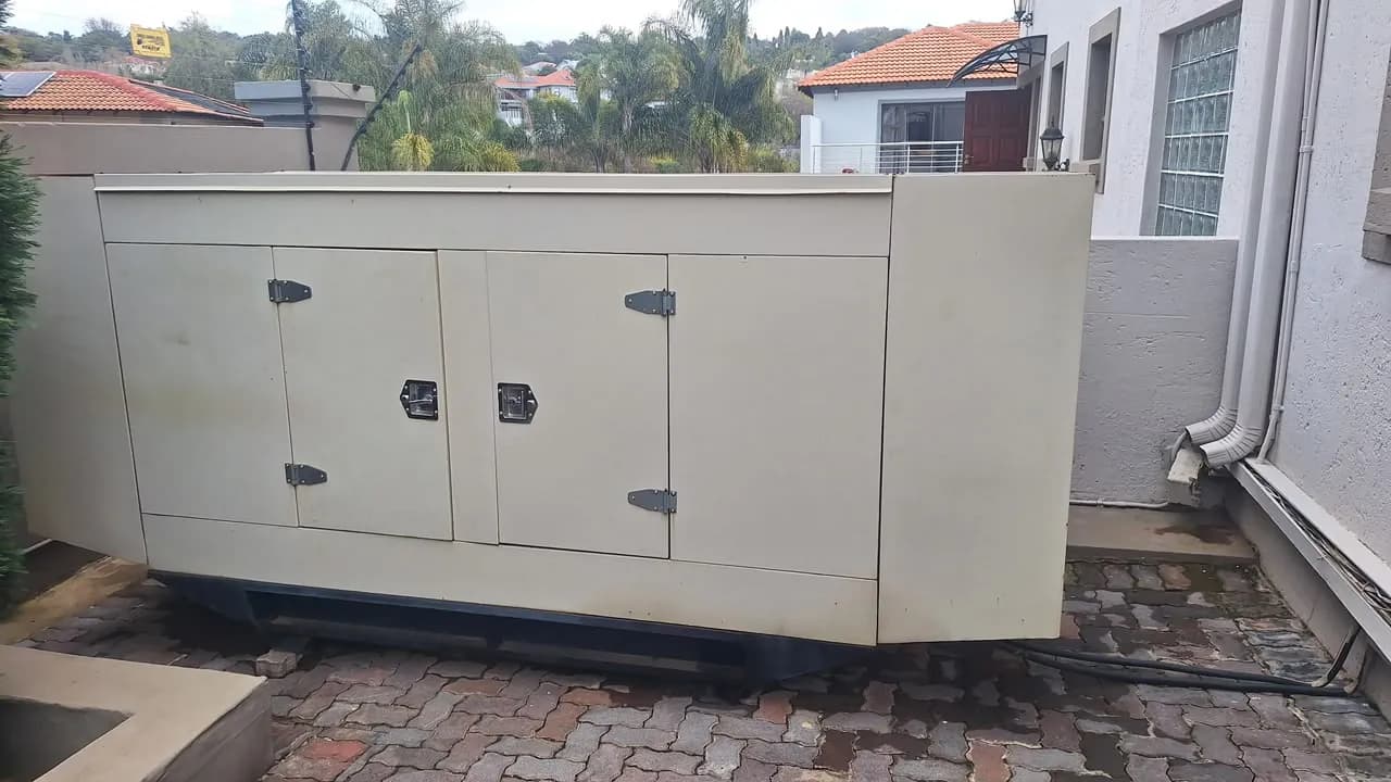 Cream canopied diesel standby generator on a paved driveway beside a house